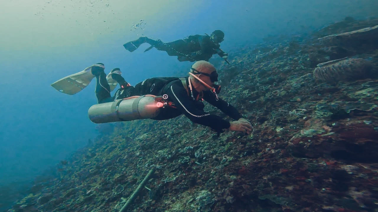 Two sidemount divers on a reef wall